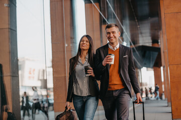 Business man and business woman talking and holding luggage traveling on a business trip, carrying fresh coffee in their hands.Business concept