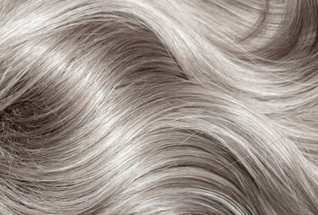 Blond hair close-up as a background. Women's long blonde hair. Beautifully styled wavy shiny curls. Hair coloring. Hairdressing procedures, extension. White hair