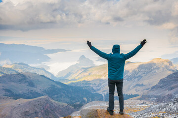 A guy with raised hands on top of a mountain. The valley is filled with fog.