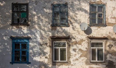 Windows on an old shabby concrete wall. An old Soviet building in the Kazakh city of Pavlodar. Window with wooden frame. Round telephysic satellite dish. Copyspace