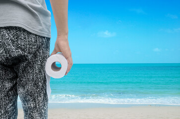 person holding toilet paper roll standing by the beach