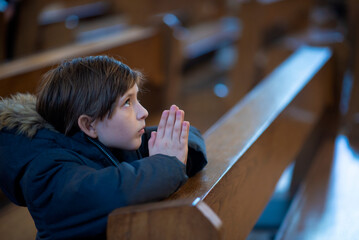a little boy in a jacket prays in a dark catholic church at a children's mass