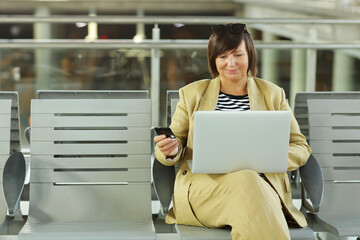 Smiling middle ages woman using credit card and laptop computer making online payment while checking flight or online check-in at airport. Mature woman holding debit card for internet banking account