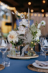 Wedding Decor. Festive table decorated with flowers on the center, candles, silverware and plates with silk napkins on dusty blue tablecloth