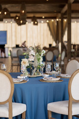 Wedding Decor. Festive table decorated with flowers on the center, candles, silverware and plates with silk napkins on dusty blue tablecloth