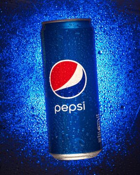 Vertical closeup of a Pepsi can on a blue background with water drops on