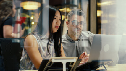 Multi-ethnic creative coworkers working on business project in modern office using laptop and digital tablet computer. Businesspeople discussing startup in e-commerce company.