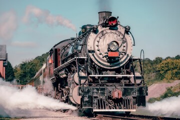 Frontal view of the vintage train creating smoke on the railways under the blue sky