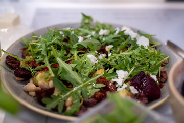
Gray plate with salad of arugula, beets, Greek cheese on a white kitchen table. Healthy vegetarian food.