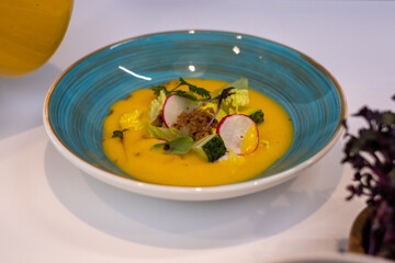blue plates with greens and vegetables, and bright yellow tomato soup. Healthy food advertisement, kitchen background.