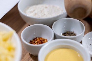 uncooked Italian pasta in white bowl on wooden table and food ingredients in bowls in blurred background. cooking process, closeup. food background. Healthy food advertising, poster for kitchen	