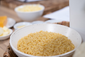 uncooked Italian pasta in white bowl on wooden table and food ingredients in bowls in blurred background. cooking process, closeup. food background. Healthy food advertising, poster for kitchen	