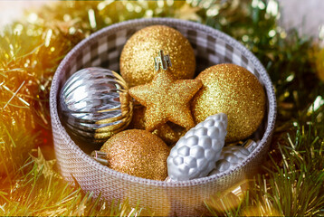 Christmas tree toys and decorations for the house. A Christmas garland's light is around. Gold and silver balls, stars, tinsel and beads are folded neatly in a box