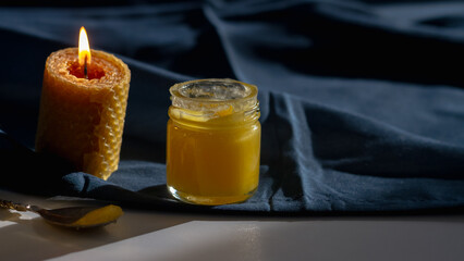 Natural bee yellow honey in a glass jar with a wax candle in the shape of a honeycomb and a spoon...