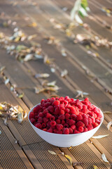 Fresh raspberries in a white bowl on the background of a wooden terrace and autumn leaves