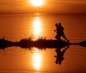 Silhouette of 2 two men running together on a sunset on lake coast. Side view of 2 men silhouette running on the sea shore. couple running on the beach at sunrise.