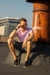 A handsome guy in denim shorts and a pink t-shirt poses beautifully in the city