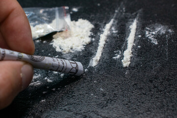 Use from a plastic bag of cocaine through a breathing tube from a hundred dollar bill, on a black...