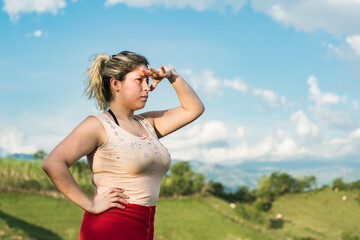 beautiful young woman, Latina university student on top of a mountain, blocking the sunlight with her left hand to get a good look at the beautiful Colombian landscapes.