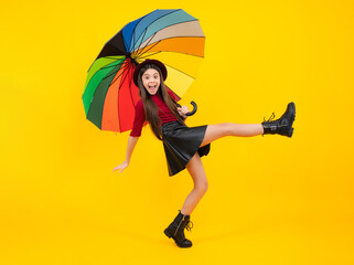 Child teenager girl with umbrella in autumn black leather skirt boots and hat isolated on yellow...