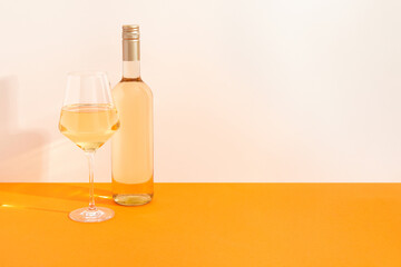 Bottle and glass of white wine on begie and orange background with deep shadows. Mock up drink with place for you lable and text