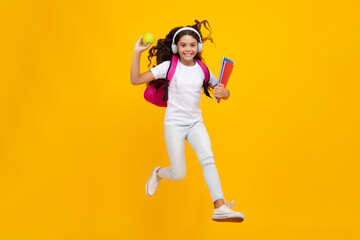 Fototapeta na wymiar Back to school. Teenager school girl with backpack and headphones hold books ready to learn. School children on isolated yellow studio background.
