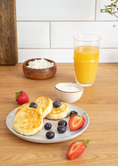 Cheesecakes or cottage cheese with fresh berries, sour cream and orange juice on a kitchen table.