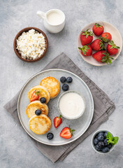 Cheesecakes or cottage cheese with fresh blerries, sour cream and milk  on a gray background. The concept of healthy and delicious breakfast.  Top view