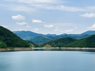 Beautiful small lake surrounded by green mountains against a blue cloudy sky