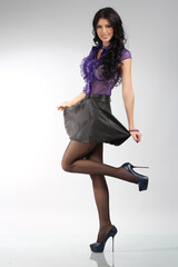 Portrait of a beautiful fashion girl brunette with big breasts in the studio in a nice lilac transparent blouse and a black leather skirt on a white background in tights