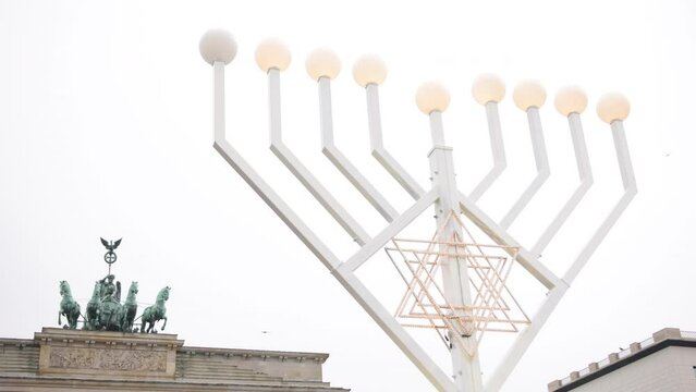 Jews celebrate Hanukkah by burning menorahs with traditional candelabras and candles in Berlin in Germany with glittering street lamps outside. Brandenburg gate in the background