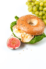 Sesame bagel stuffed with egg and salad on a white background. Delicious and hearty breakfast with figs and grapes. Creative concept of food