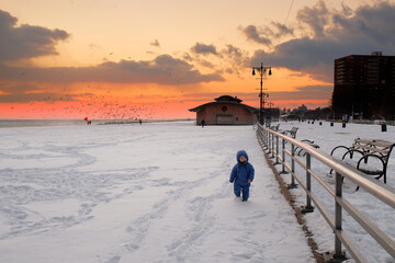 cute baby toddler is running on a beach covered with snow at susnset