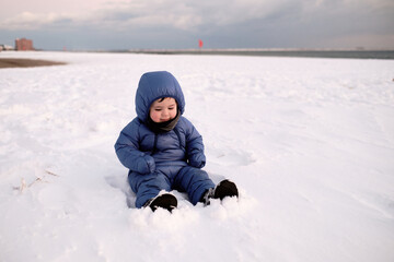 Fototapeta na wymiar cute baby toddler is playing on a beach covered with snow