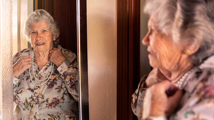 Happy cheerful caucasian 90s grandmother in elegant clothes looking at mirror.