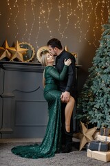 Romantic couple standing near Christmas tree wearing magnificent clothes