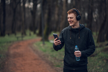 Redhead young man using a smartphone while running in the forest