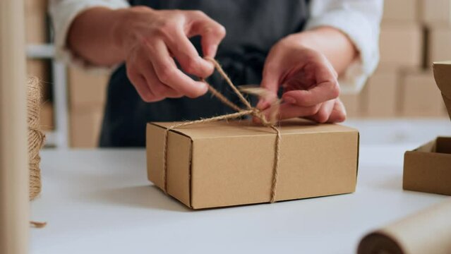 Small business owners packing cardboard boxes for customers who make online orders through the Internet, e-commerce, packaging cardboard boxes tying jute string rope
