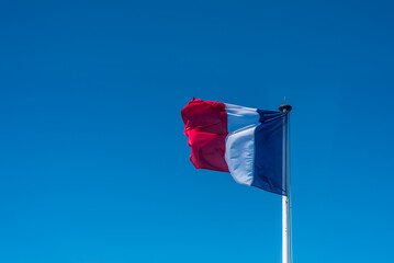 French flag on the pole over a blue sky. 