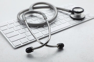 Computer keyboard with stethoscope on white table, closeup