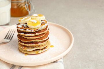 Plate of banana pancakes with honey and powdered sugar served on light table, closeup. Space for text