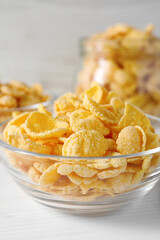 Glass bowl of tasty crispy corn flakes on white wooden table, closeup