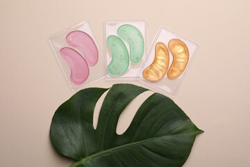 Under eye patches and tropical leaf on beige background, flat lay. Cosmetic product