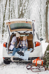 Woman and her daughter sitting in open car's trunk in winter forest
