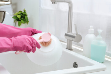 Woman washing bowl with brush above sink in kitchen, closeup