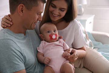 Happy couple holding their cute little baby with pacifier at home
