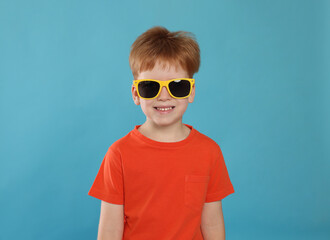 Cute little boy with sunglasses on light blue background