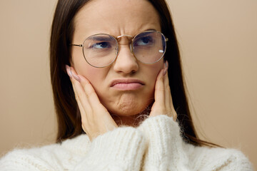 an emotional, funny woman stands in glasses for vision on a beige background holding her glasses with her hands and makes a very funny face, frowning her eyebrows and lowering the corners of her lips