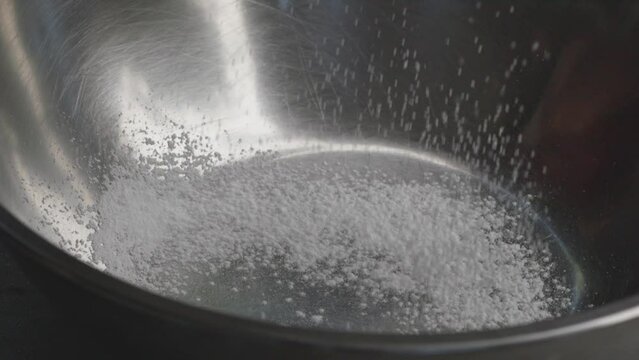 Close-up of a fine curtain of white cake flour falling through a flour sifter in the kitchen., Slow motion

