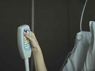 The hand of a young caucasian male holds a medical bedside remote control and presses a button